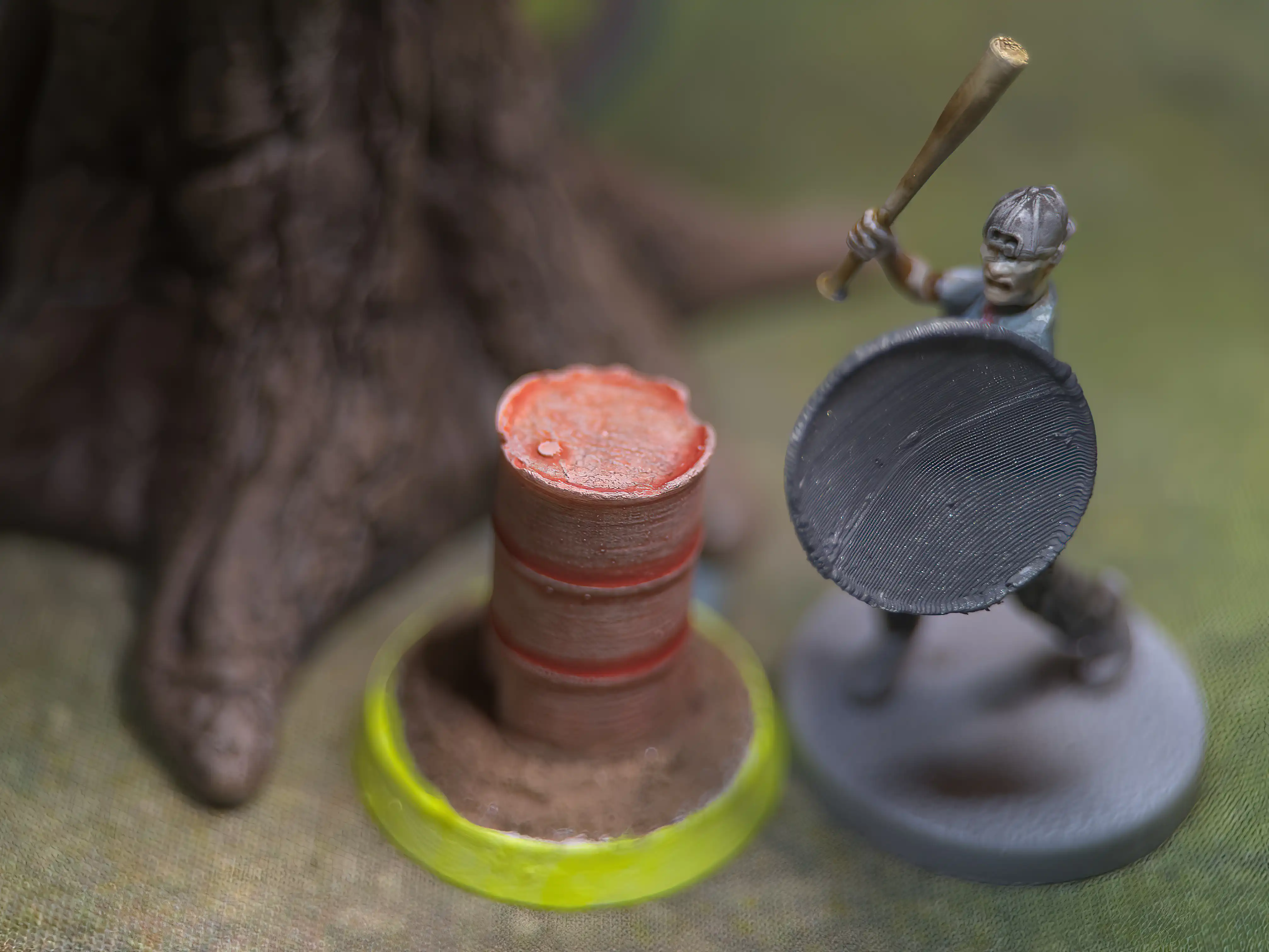 close-up of a miniature carrying a baseball bat and standing next to a resource token; they are surrounded by trees